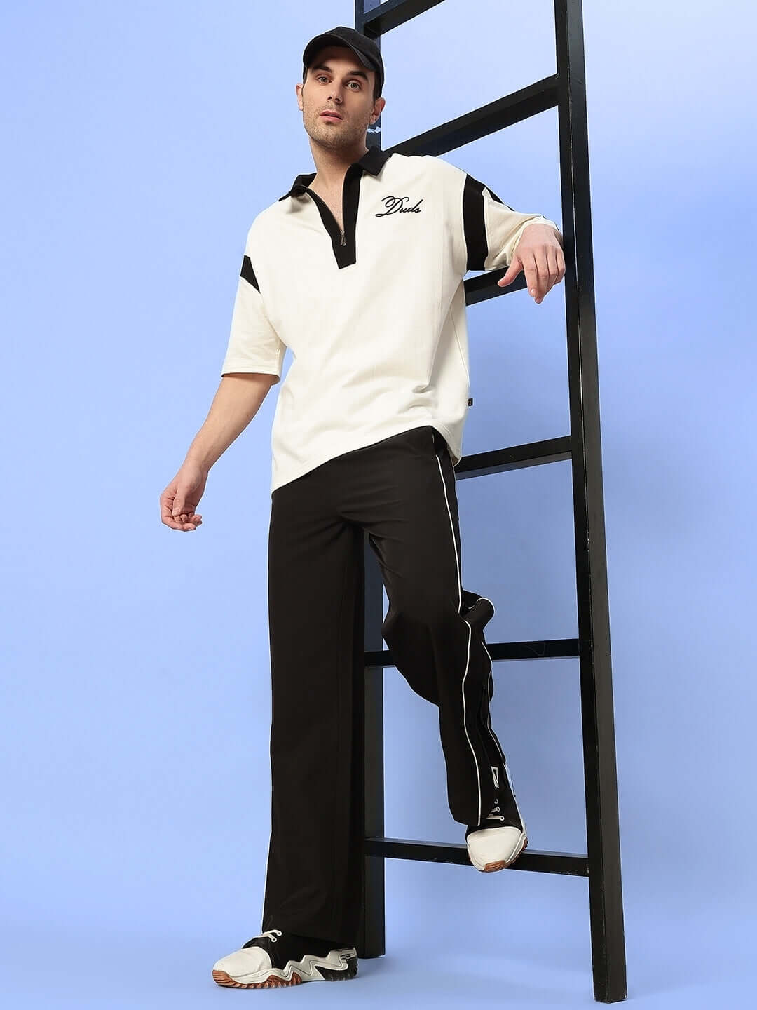 Model wearing Relight Relaxed-Fit Joggers in black with a white polo shirt, standing by a ladder, showcasing fashionable streetwear style.