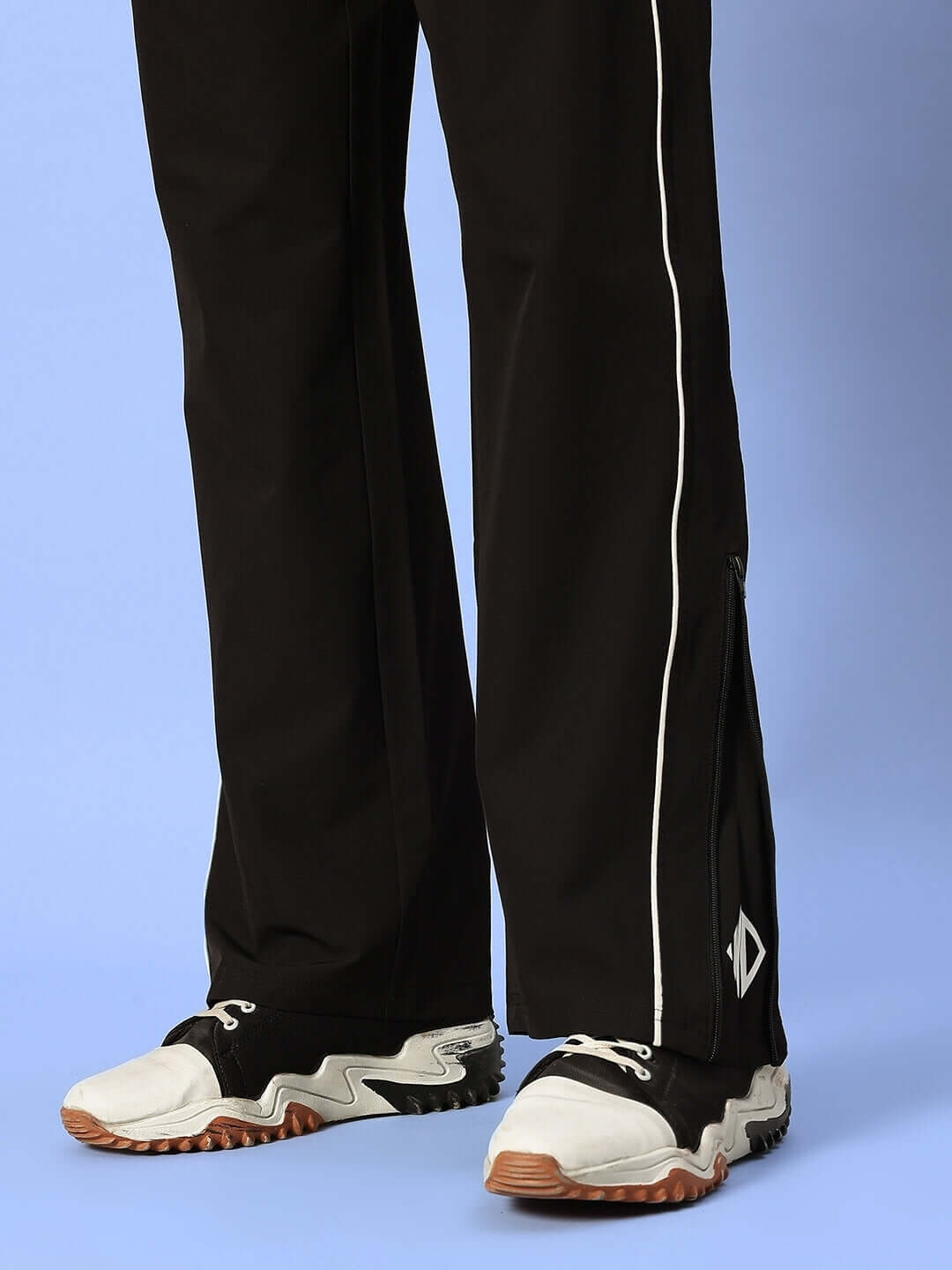 Black relaxed-fit joggers by RELIGHT with white piping detail, shown with white and black sneakers on a blue background.