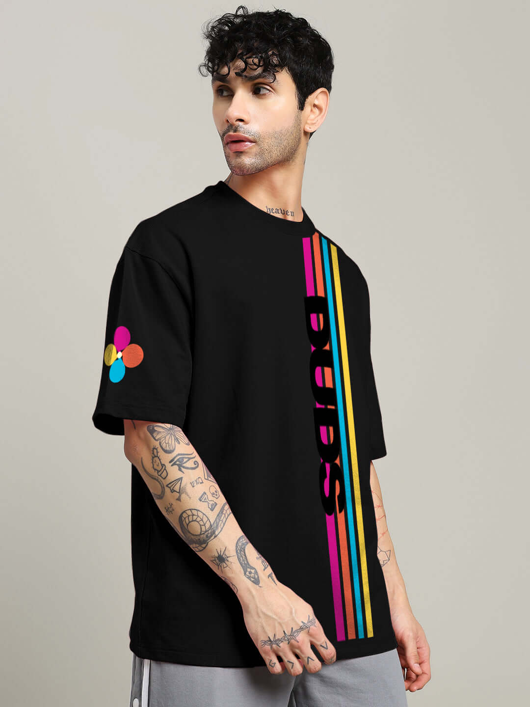 Model wearing RETRO STRIPES OVERSIZED T-SHIRT BLACK with colorful vertical stripes and tattoos displayed on arms.