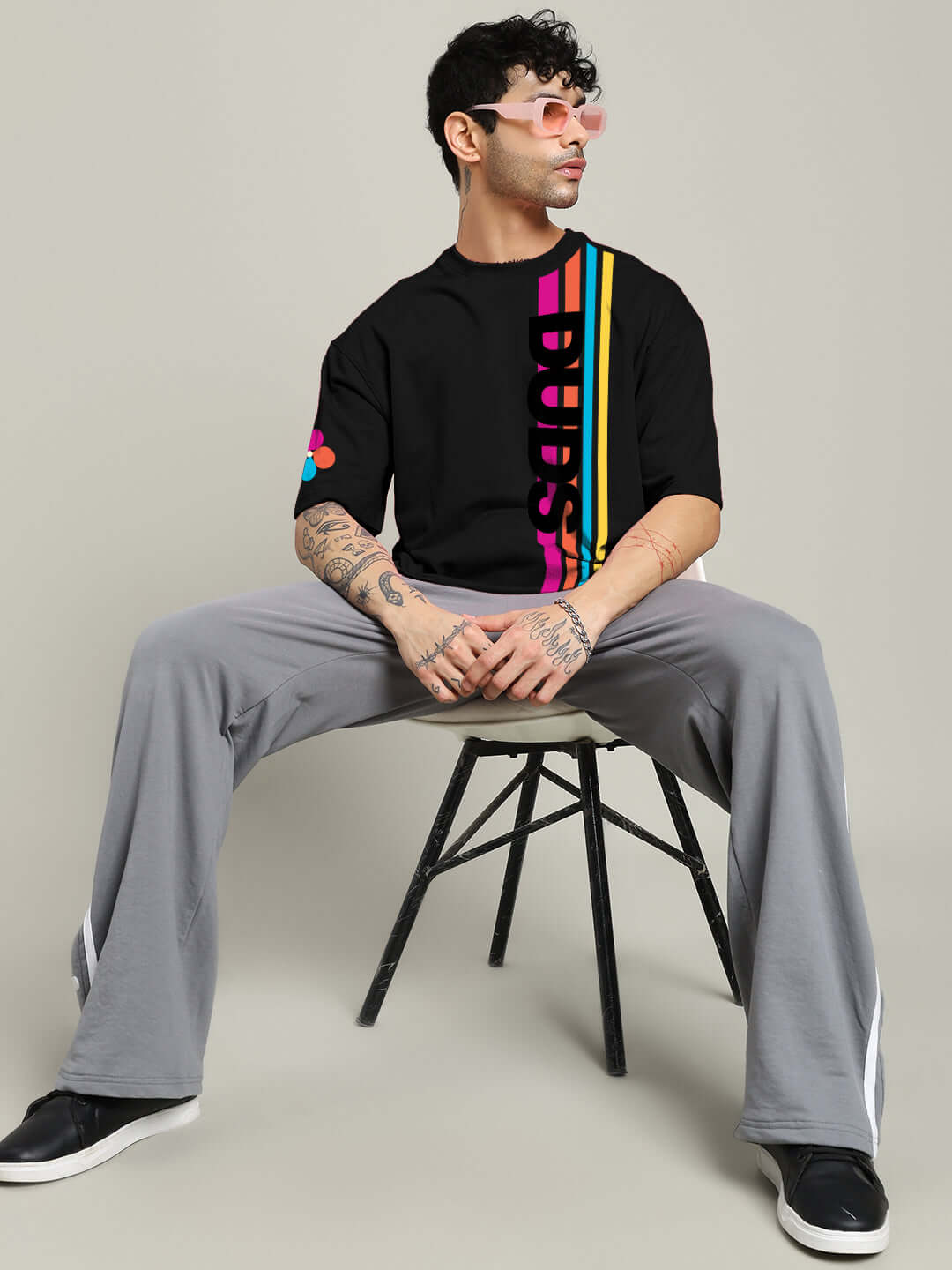Model wearing black retro stripes oversized t-shirt with pink and yellow design, paired with gray pants and black sneakers.