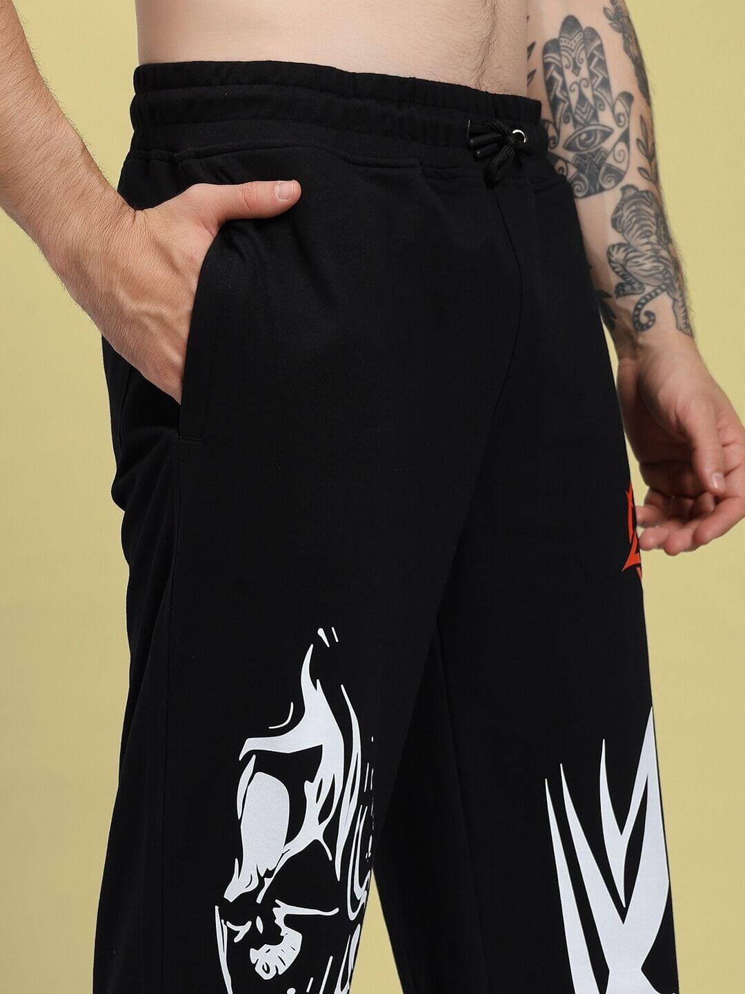 Person wearing RIFT RELAXED FIT JOGGER IN BLACK with graphic design, showcasing front pocket and tattoo on arm.