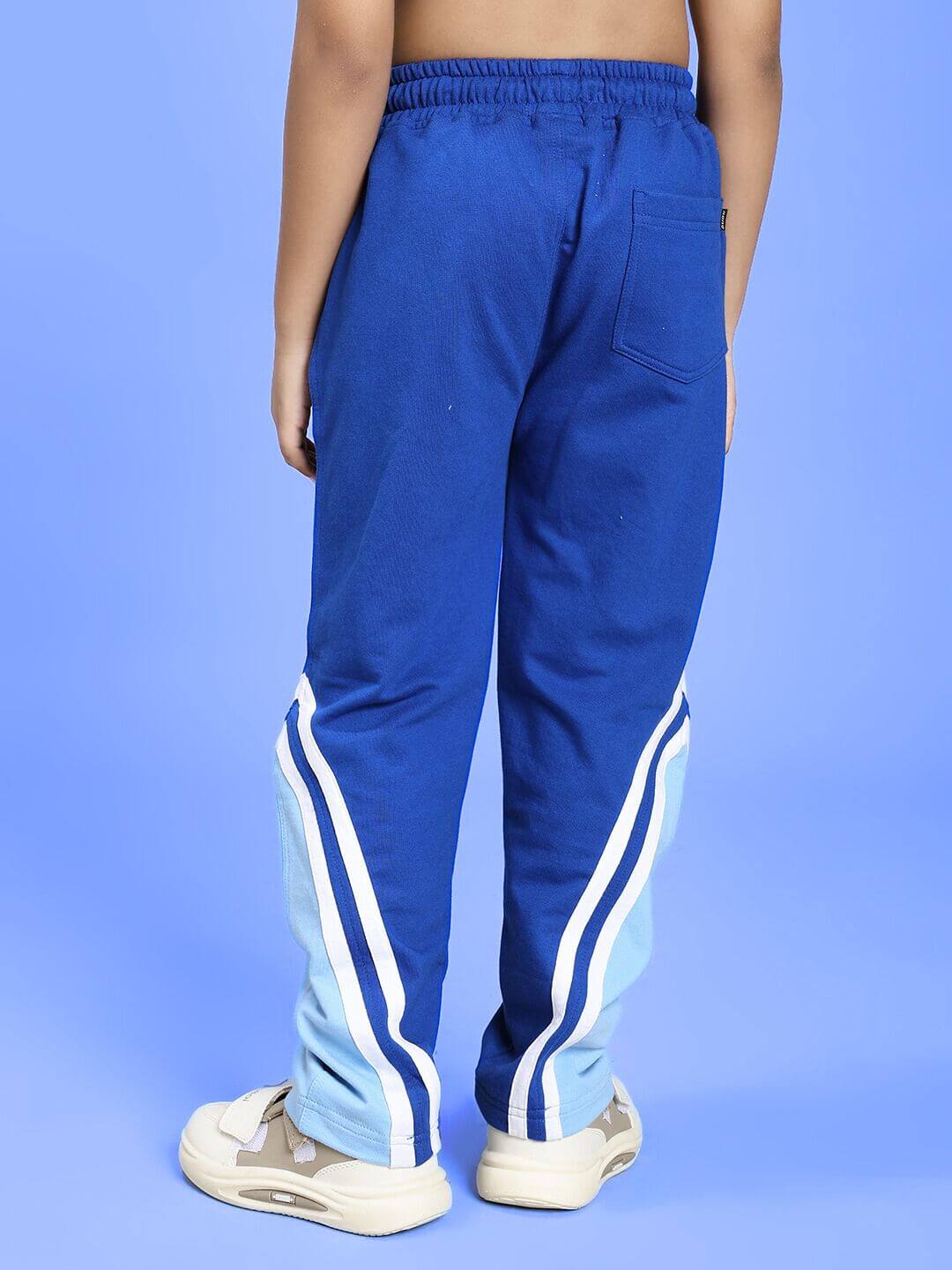 Back view of kid wearing RIO ONE RELAXED FIT JOGGER FOR BOYS AND GIRLS BLUE with white sneakers on a blue background.