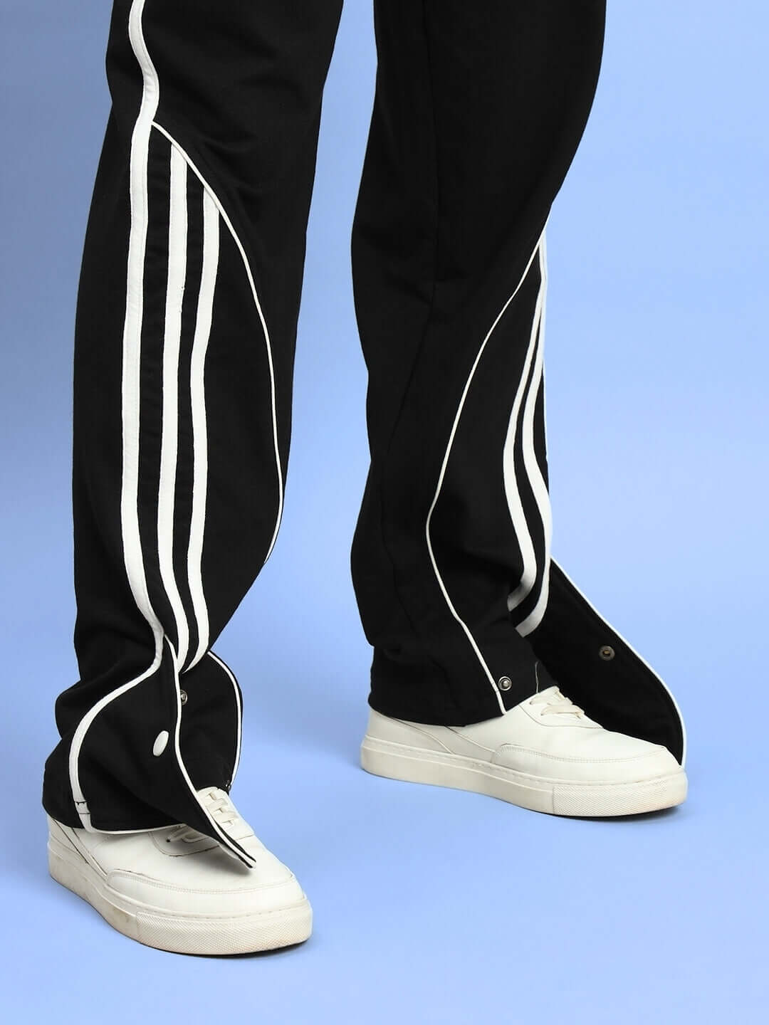 Black ripple contrast joggers with white side stripes and buttoned hems, paired with white sneakers on a light blue background.