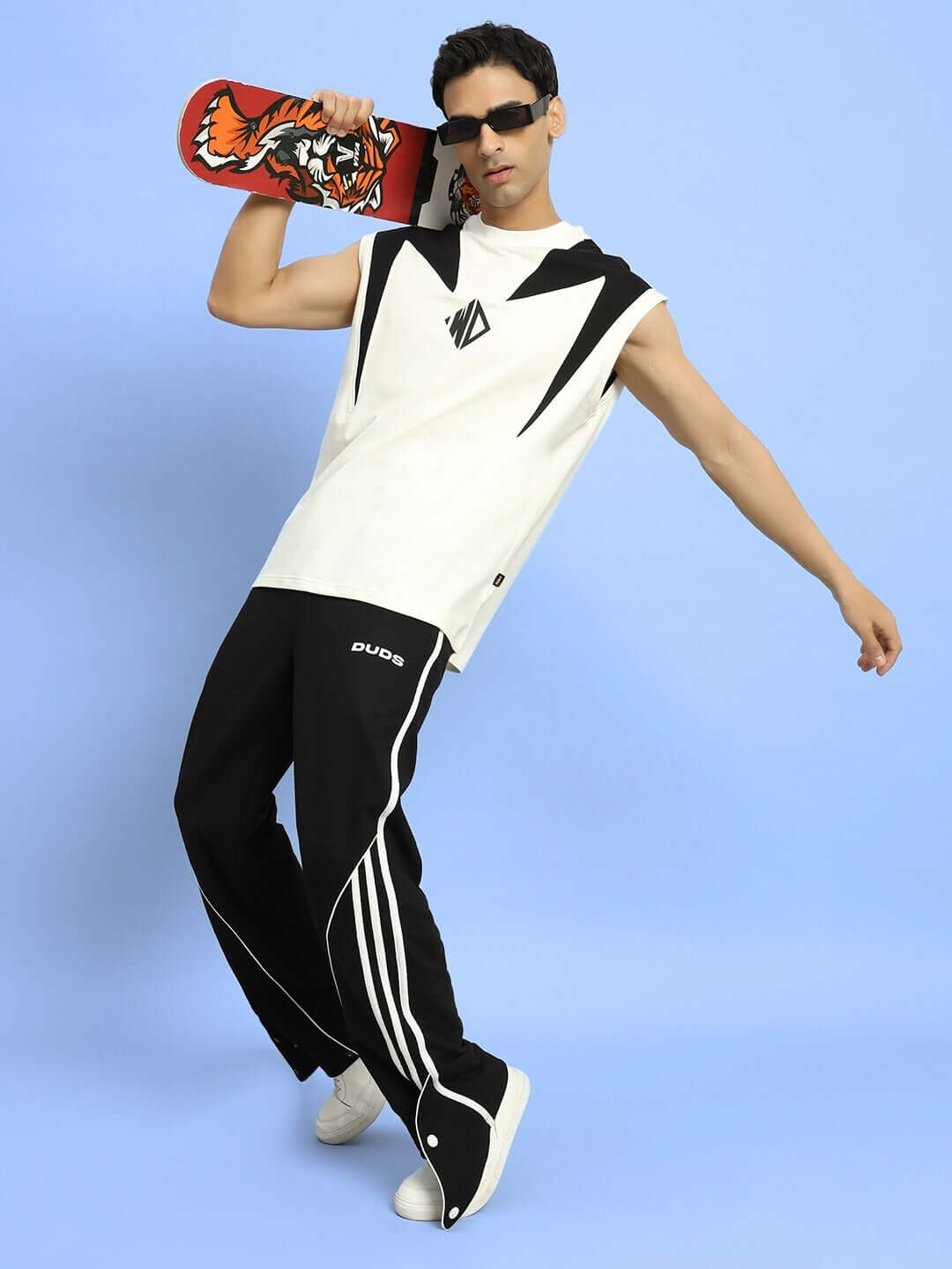 Model wearing black Ripple Contrast Joggers by DUDS, holding skateboard, showcasing casual streetwear fashion against blue backdrop.
