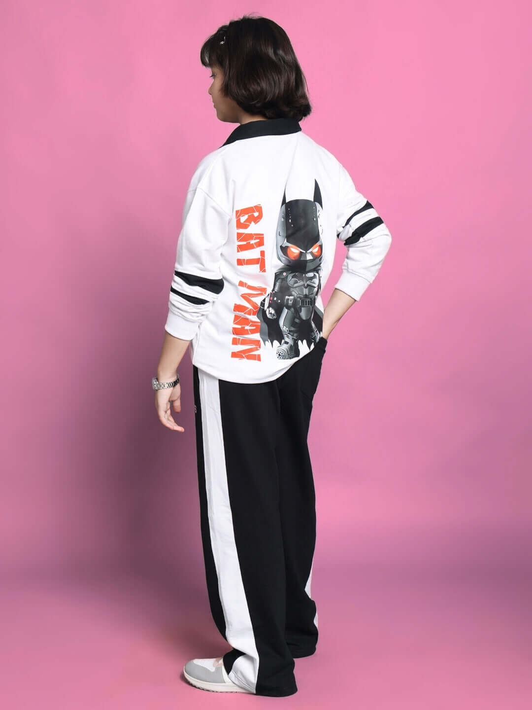 Child in Batman-themed oversized tracksuit with black and white stripes posing against a pink backdrop.