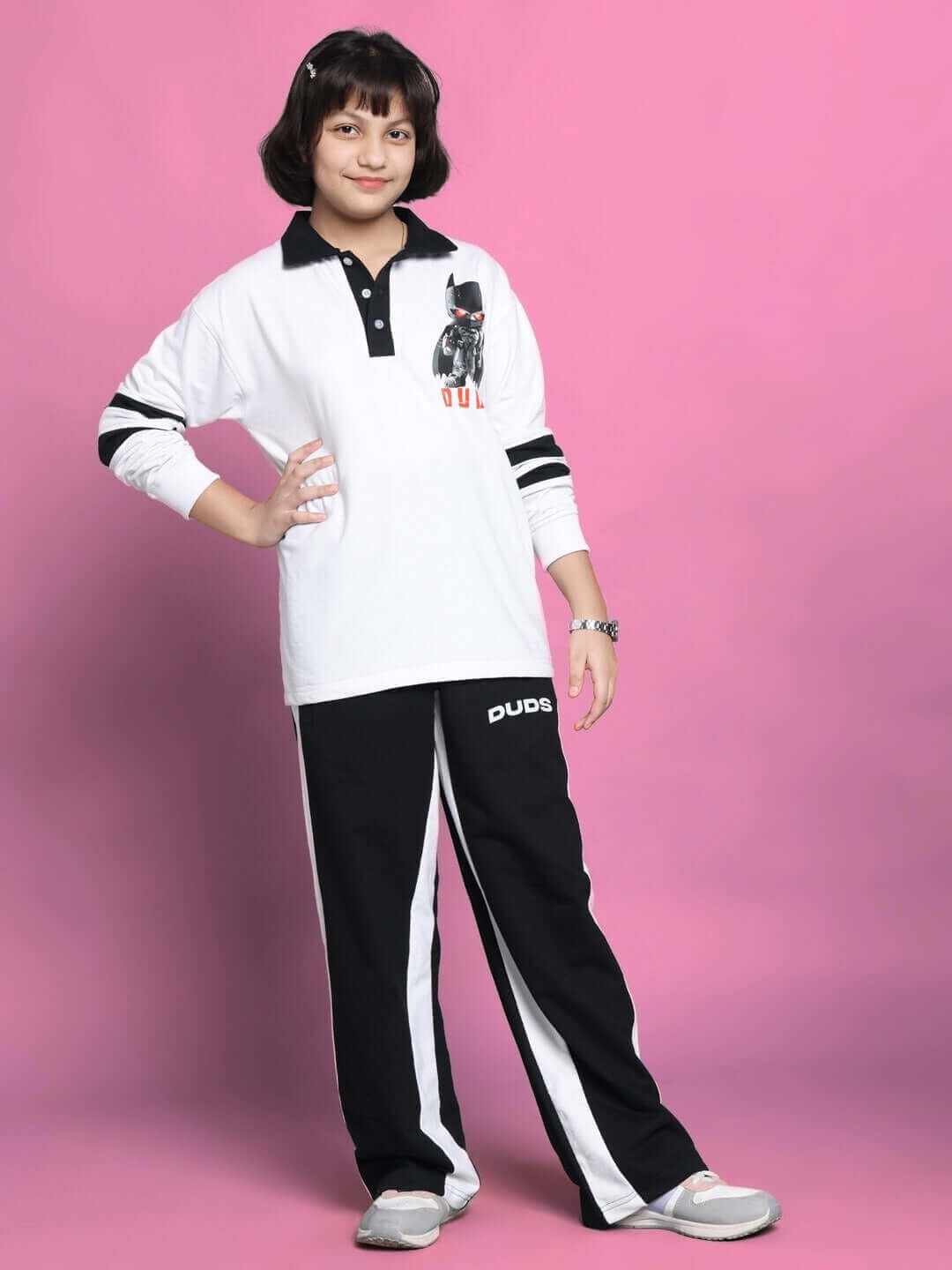 Child wearing a white oversized Robin sweatshirt with black accents, styled with black and white pants, standing against a pink background.