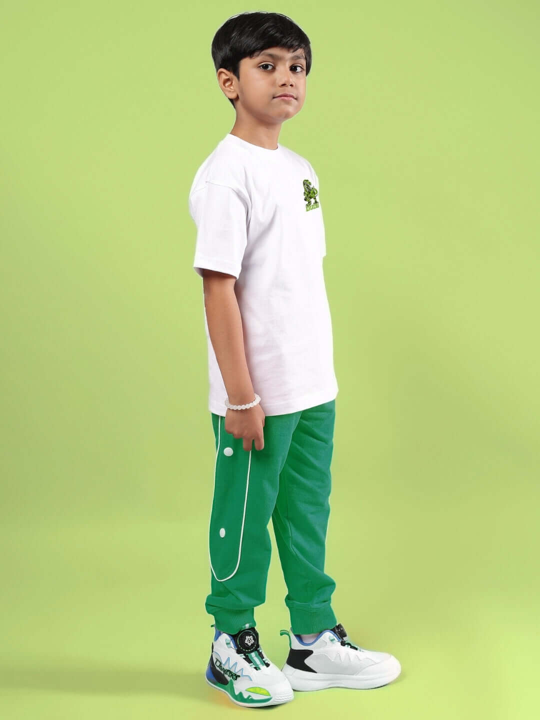 Young boy wearing ROBO REX CO-ORD FOR BOYS & GIRLS WHITE-GREEN outfit, featuring a white t-shirt and green pants, standing against a green background.