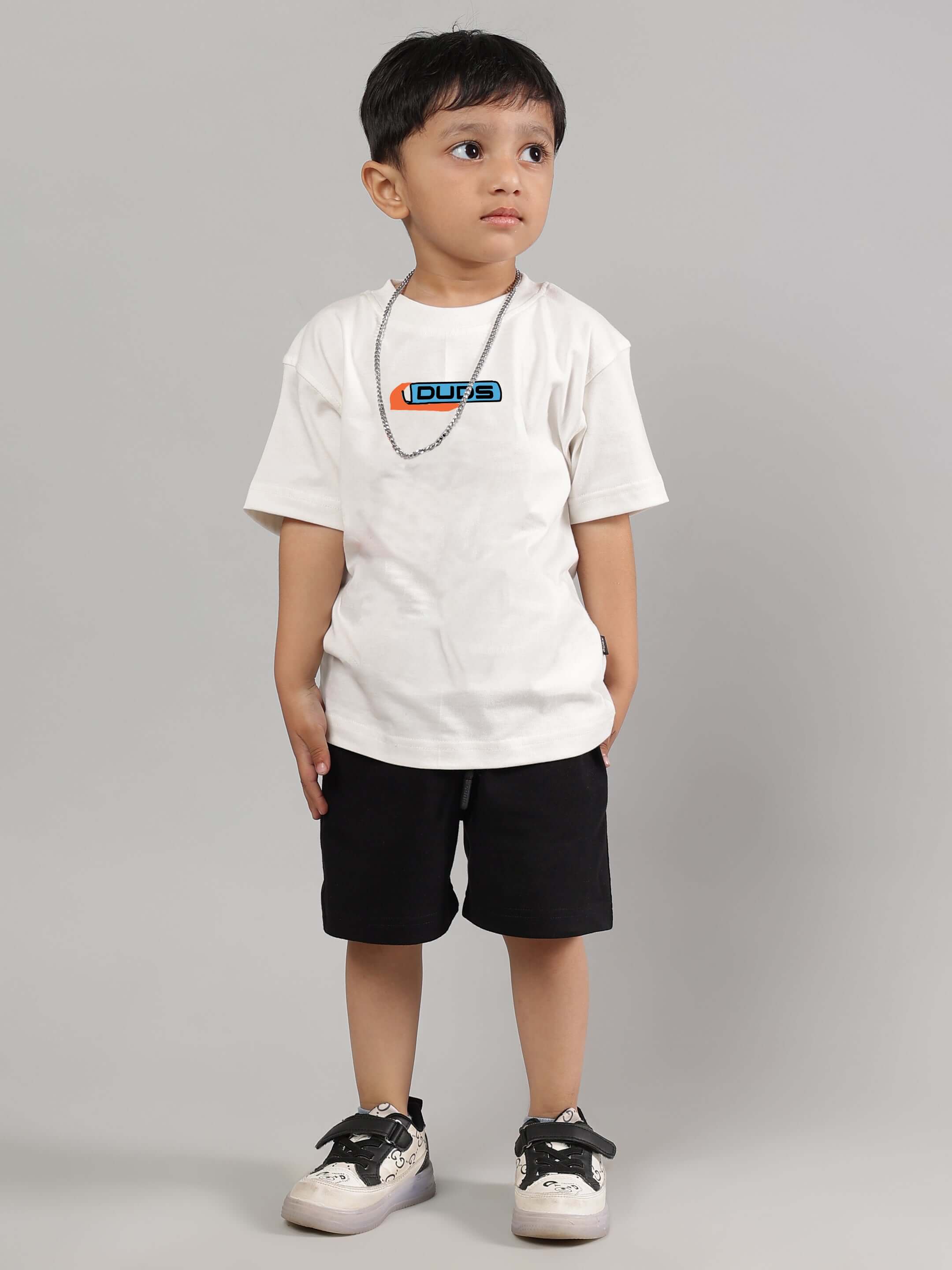 Child wearing a DUDS branded white Robo Shark T-shirt for boys and girls, paired with black shorts and sneakers.