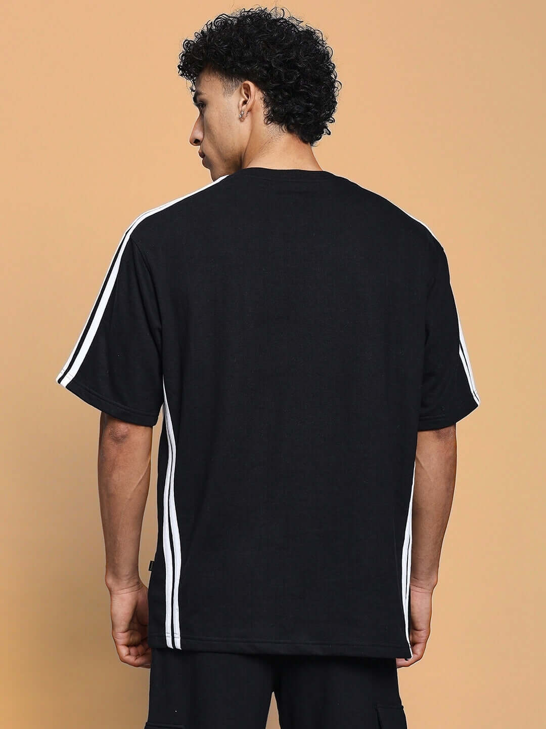 Back view of model wearing RODDY OVER-SIZED CLASSIC T-SHIRT BLACK with white stripes on sleeves