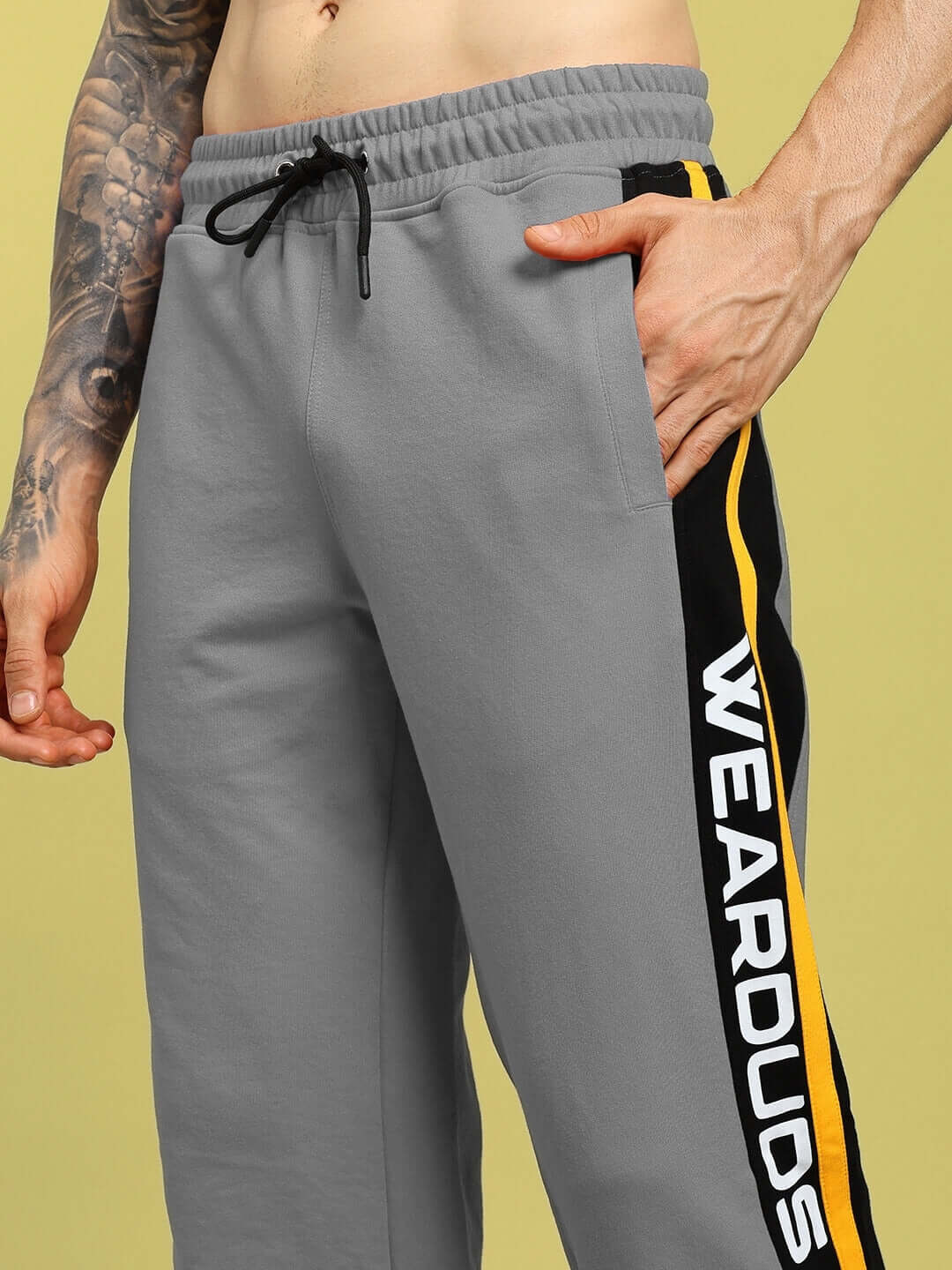 Man wearing grey ROGER relaxed-fit joggers with side stripe and "WEARDUDS" logo, showcasing comfortable and stylish design.