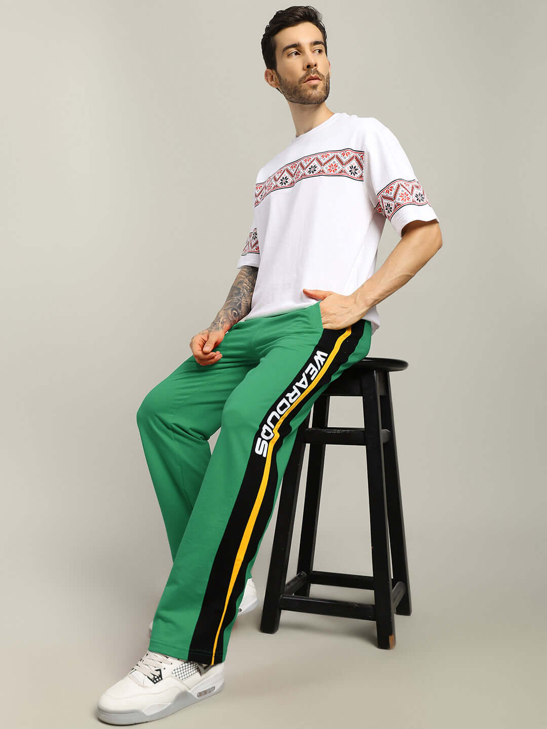 Man wearing ROGER RELAXED-FIT JOGGERS GREEN with a white printed tee, sitting on a stool.
