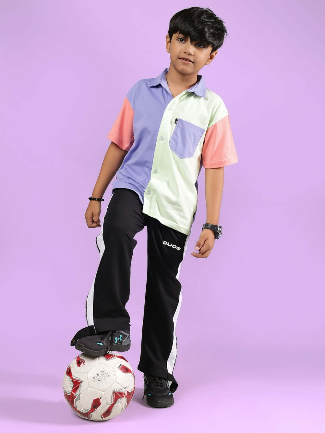 Boy wearing ROMAN CO-ORD FOR BOYS & GIRLS MULTI-BLACK set with soccer ball, showcasing trendy and sporty look on purple background.