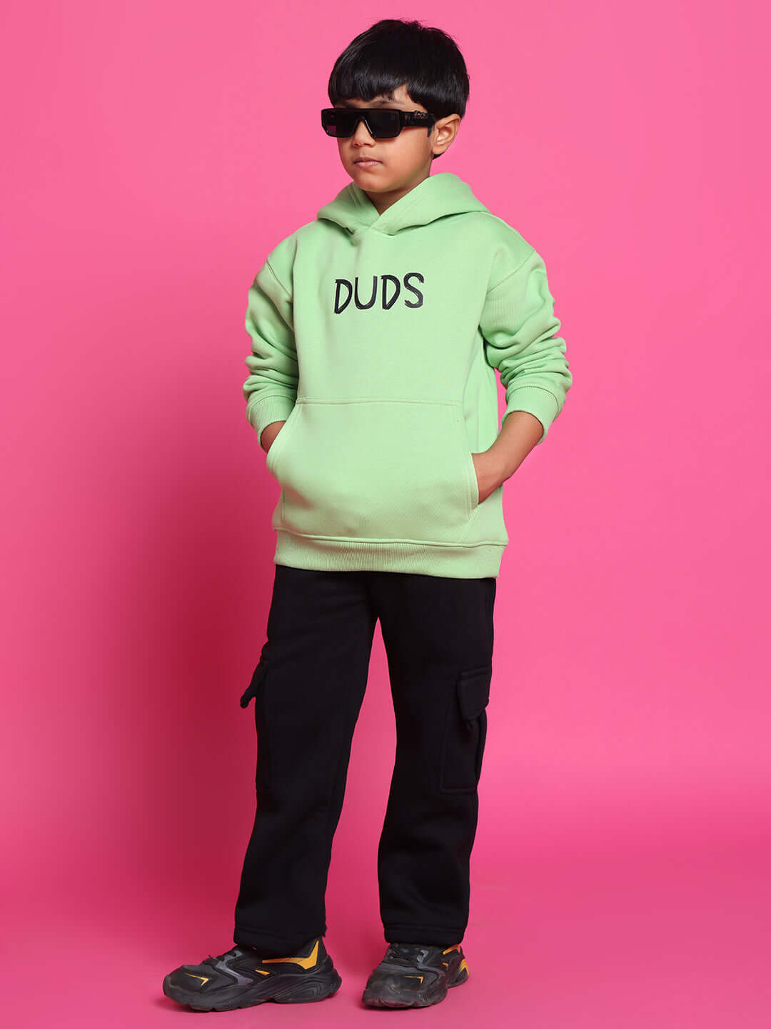 Child wearing ROOAR CO-ORD FOR BOYS GIRLS NEON GREEN outfit with hoodie, hands in pockets, and sunglasses against pink background.