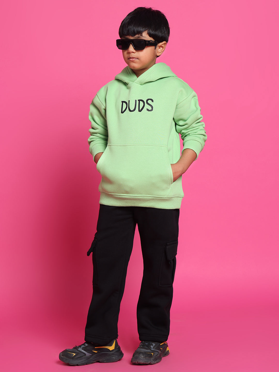 Child wearing ROOAR CO-ORD FOR BOYS GIRLS NEON GREEN outfit with hoodie, hands in pockets, and sunglasses against pink background.