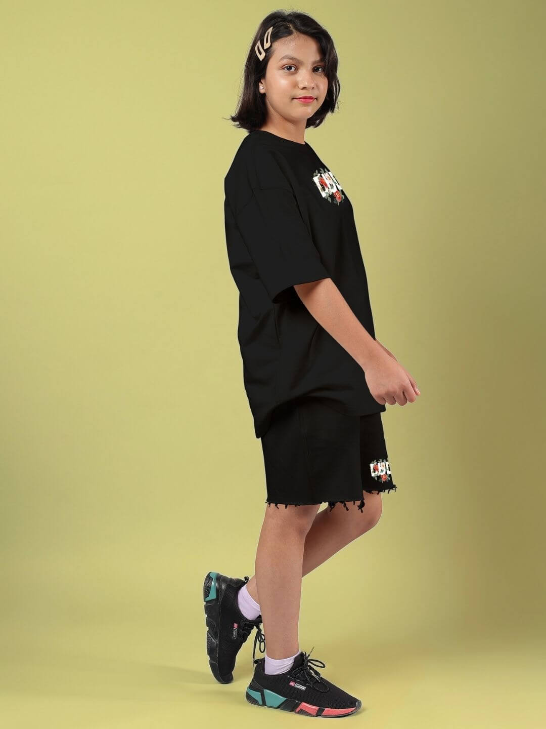 Child wearing ROSE CHARM CO-ORD FOR BOYS AND GIRLS BLACK, featuring black top and shorts with rose charm on a yellow background.