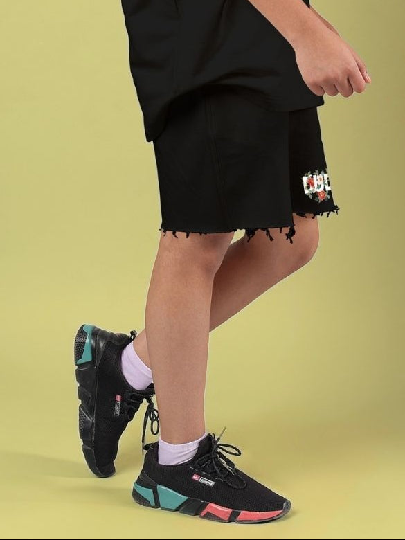 Child wearing ROSE CHARM SHORTS FOR BOYS AND GIRLS BLACK with sneakers standing indoors