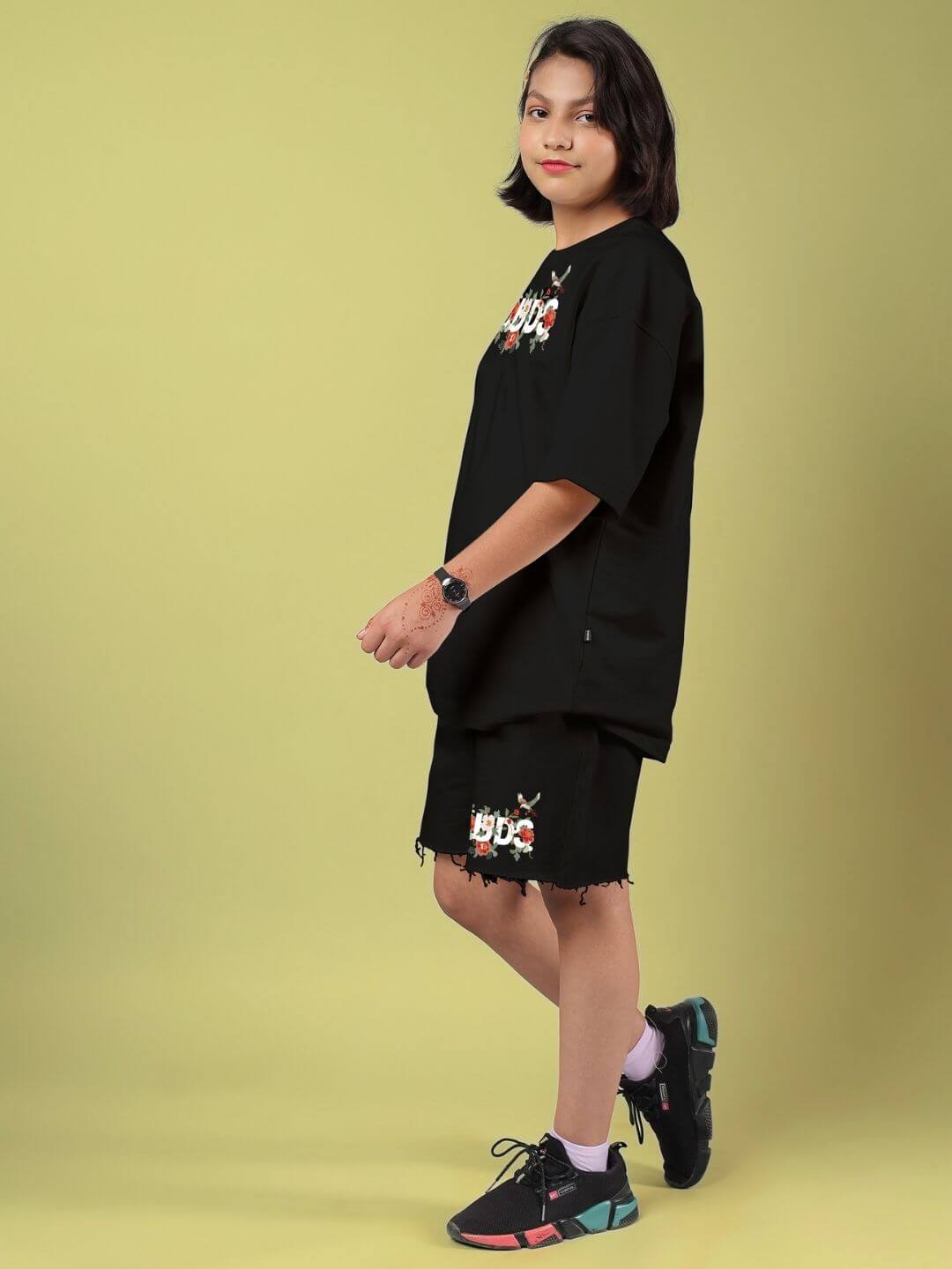 Child wearing ROSE CHARM CO-ORD FOR BOYS AND GIRLS BLACK with rose charm detail on a yellow background, showcasing unisex streetwear style.
