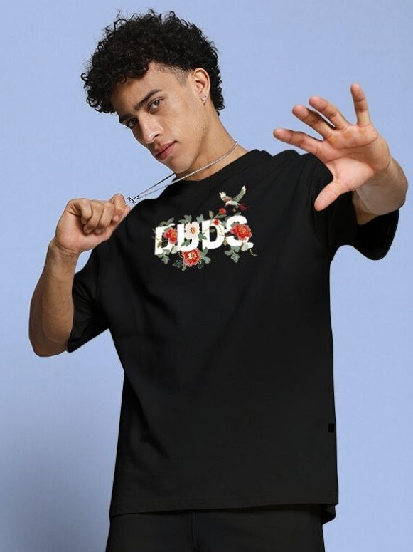Stylish model wearing ROSE CHARM OVER-SIZED T-SHIRT BLACK with floral design on the front.