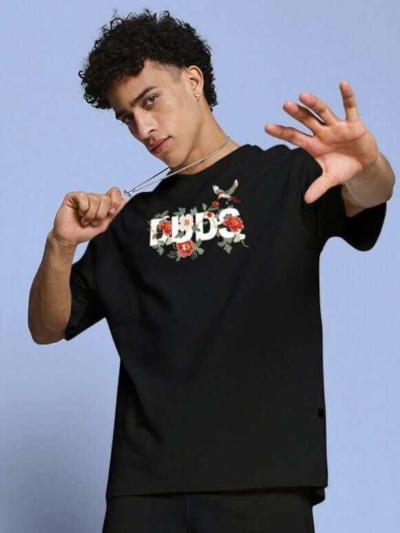 ROSE CHARM OVER-SIZED T-SHIRT BLACK featuring a bold rose graphic, worn by a model for a street style look.