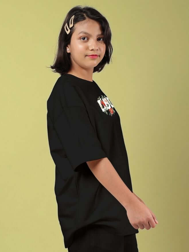 Child wearing ROSE CHARM OVERSIZED T-SHIRT FOR BOYS AND GIRLS BLACK with rose detail against a light background.