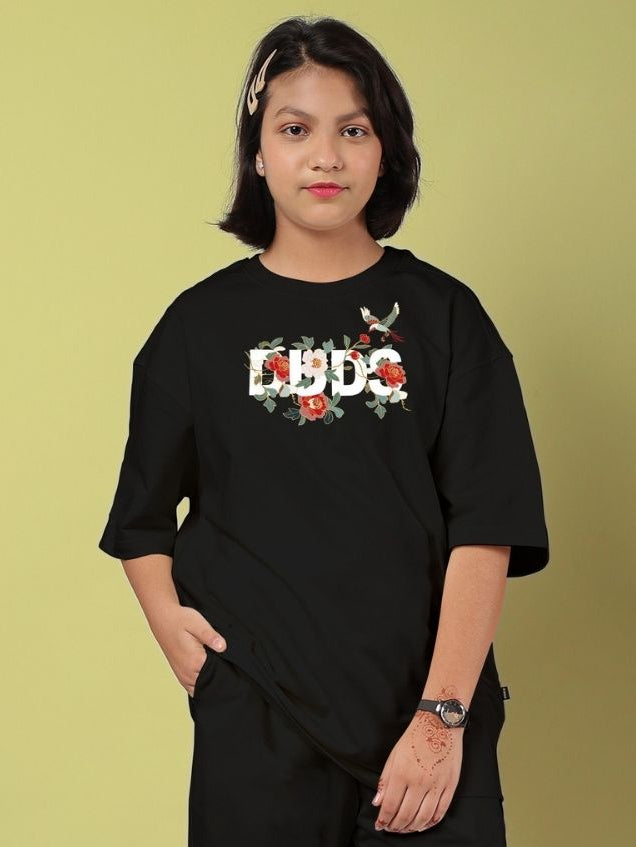 Teen wearing ROSE CHARM OVERSIZED T-SHIRT FOR BOYS AND GIRLS BLACK standing against a yellow background.