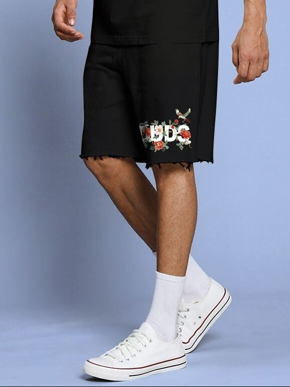 Man wearing ROSE CHARM RELAXED FIT SHORTS BLACK with embroidered design, paired with white sneakers and socks.