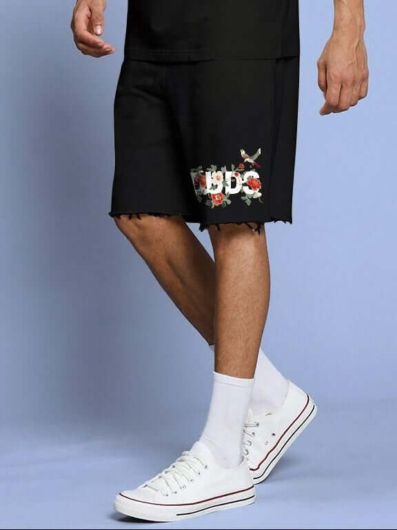 Man wearing ROSE CHARM RELAXED FIT SHORTS BLACK with floral detailing, showcasing comfort and style in casual fashion.