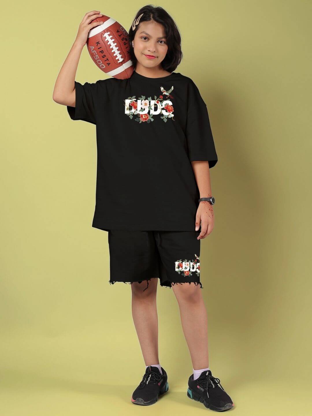 Child wearing ROSE CHARM SHORTS FOR BOYS AND GIRLS BLACK holding a football, showcasing unisex casual style.