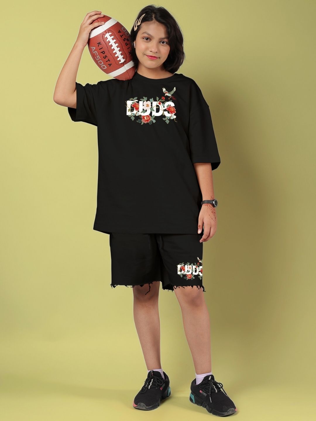 Child wearing ROSE CHARM OVERSIZED T-SHIRT FOR BOYS AND GIRLS BLACK, holding a football, showcasing street-chic style.