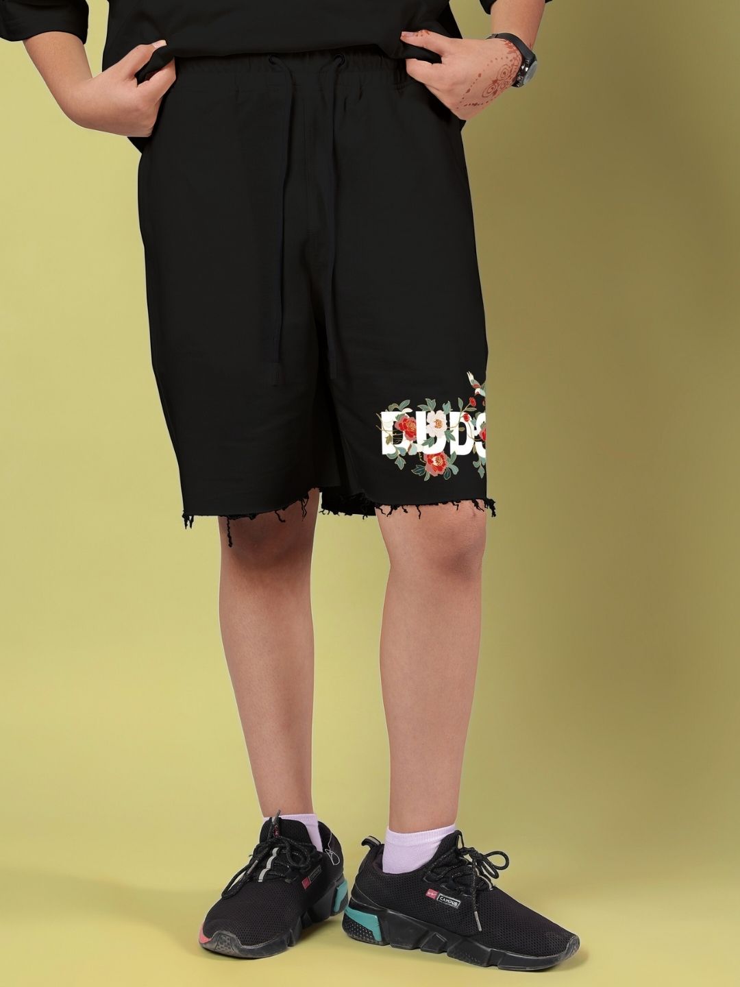 Boy wearing ROSE CHARM SHORTS FOR BOYS AND GIRLS BLACK with floral design, standing against a light background with hands in pockets.