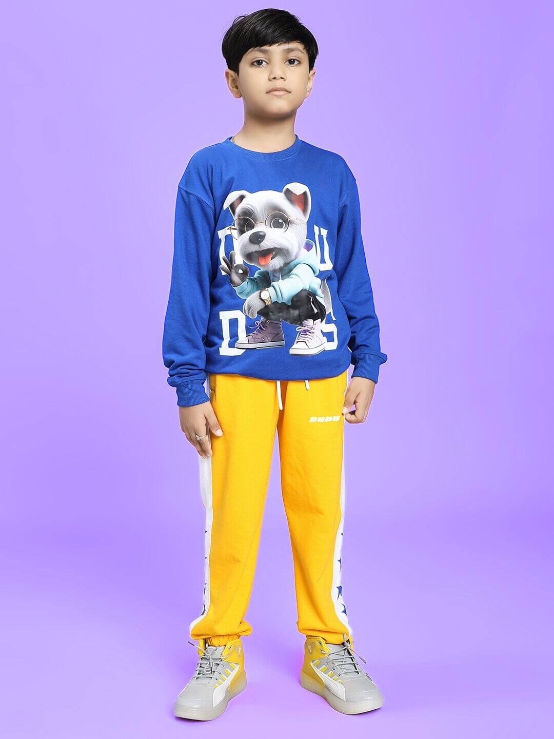 Child wearing ROX PRIMER JOGGER FOR BOYS AND GIRLS YELLOW WHITE, paired with a blue cartoon sweatshirt, standing against a purple background.