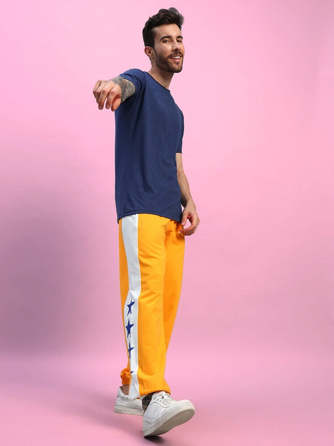Man wearing ROX PRIMER Relaxed Fit Joggers in orange-white with stars, standing against a pink background.