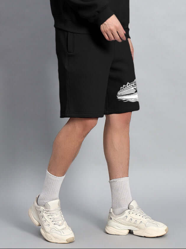 Model wearing RULE THE WORLD FLEECE SHORTS BLACK with sneakers and socks, showcasing streetwear fashion style.