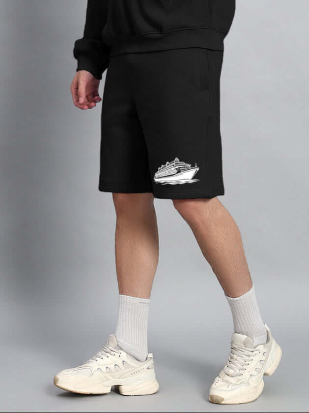 Model wearing black shorts with cruise ship graphic and white sneakers, paired with oversized hoodie. Stylish casual streetwear look.