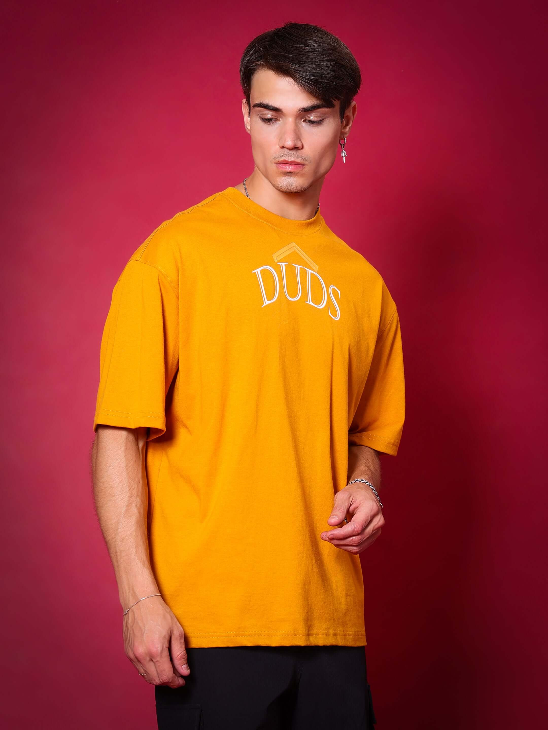 Man wearing mustard SAKURA BLOSSOM oversized t-shirt from DUDS against a red background
