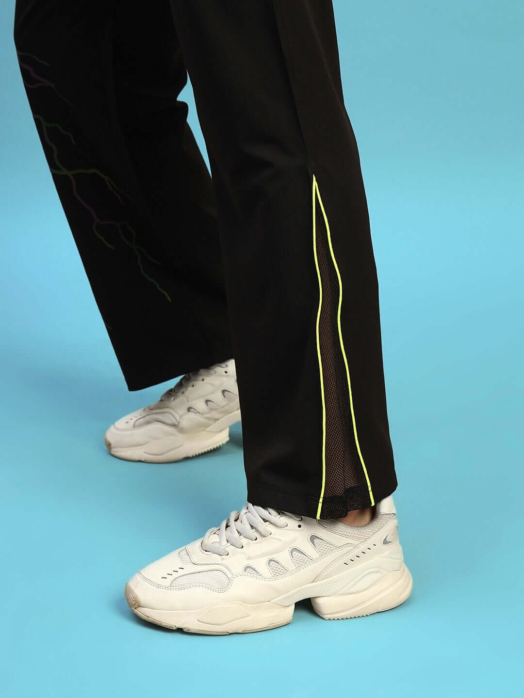 Close-up of Salvo Reflector Co-Ord Set pants in black sports polyester with side slit, paired with white sneakers, on a blue background.