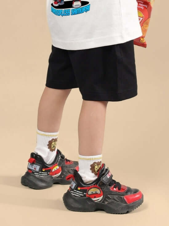 Child wearing SAMURAI PRINTED SHORTS FOR BOYS & GIRLS BLACK with colorful sneakers and cartoon socks.