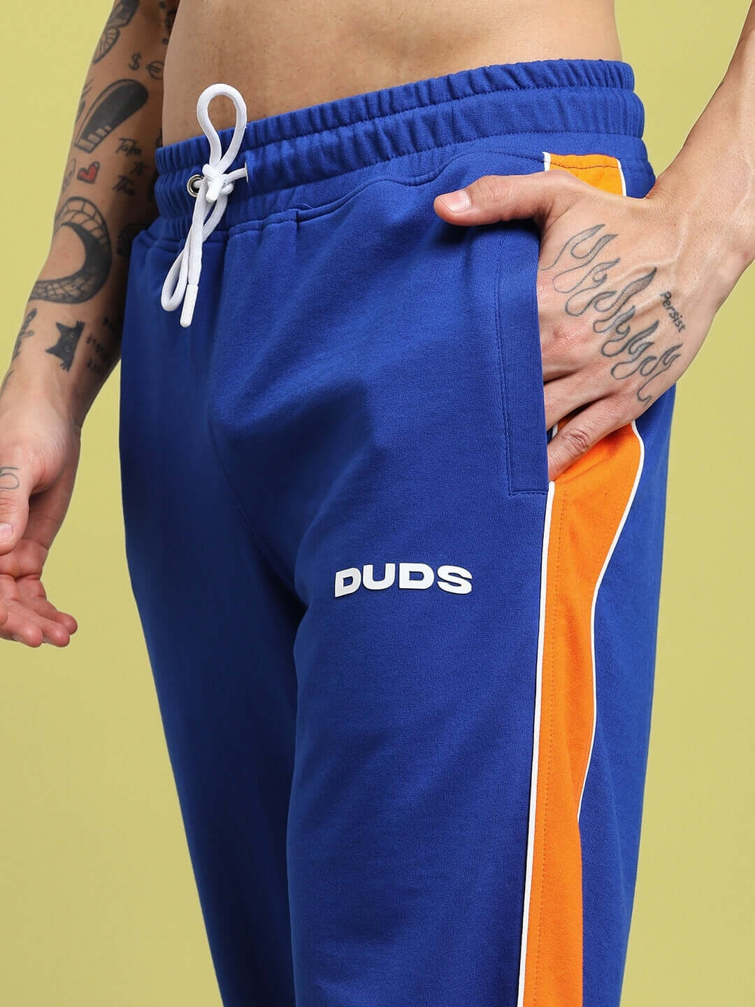 Close-up of SANFORD STRIPE JOGGERS BLUE with orange stripe, worn by tattooed model, highlighting comfortable fit for active wear.