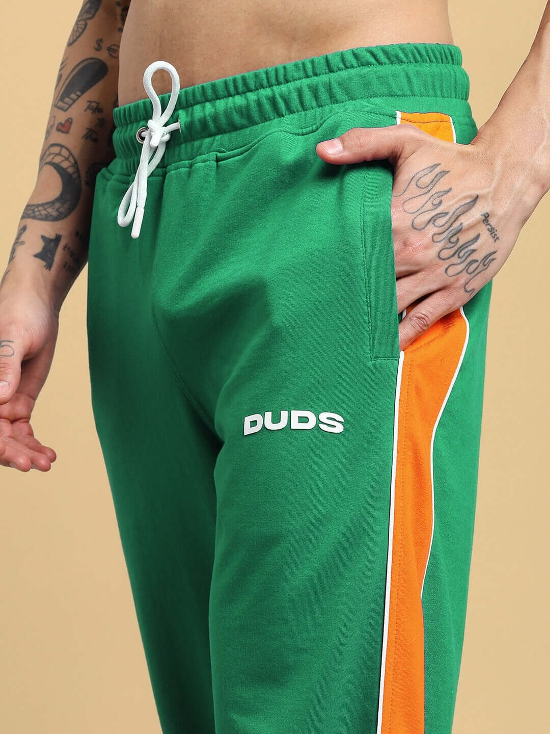 Person wearing SANFORD STRIPE JOGGERS IN GREEN with orange side stripe, showcasing sporty athleisure style.
