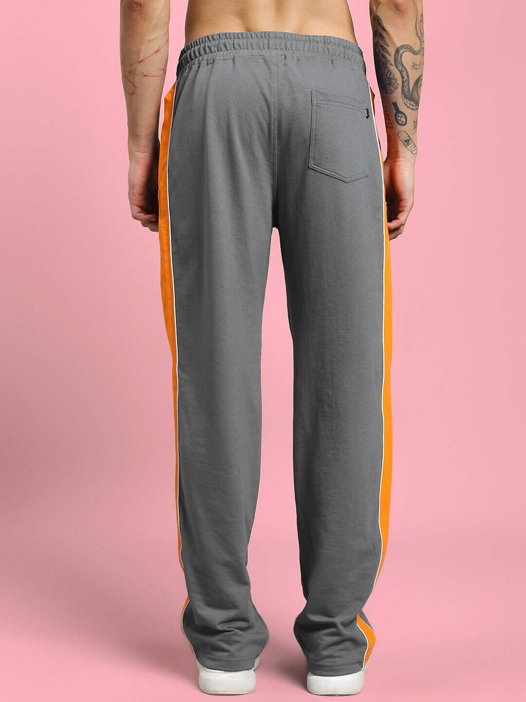 Rear view of SANFORD STRIPE JOGGERS IN GREY with bold side stripes, showcasing modern streetwear style on a pink background.