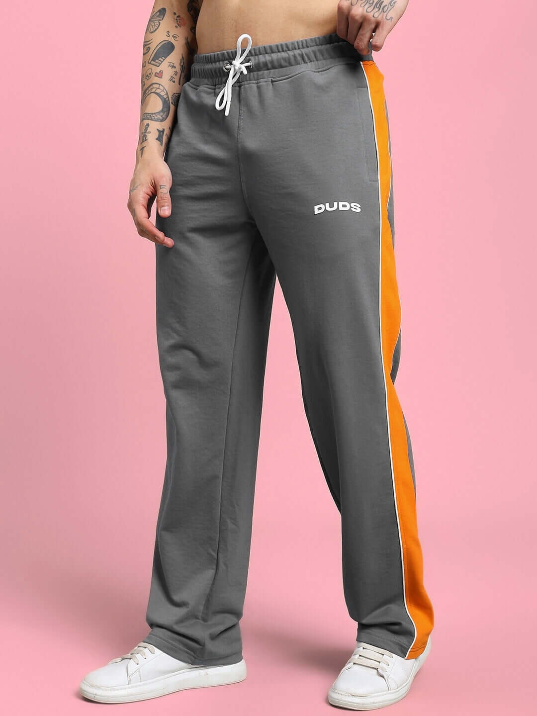 Man wearing SANFORD STRIPE JOGGERS IN GREY with bold orange side stripes, showcasing modern athleisure style against a pink background.