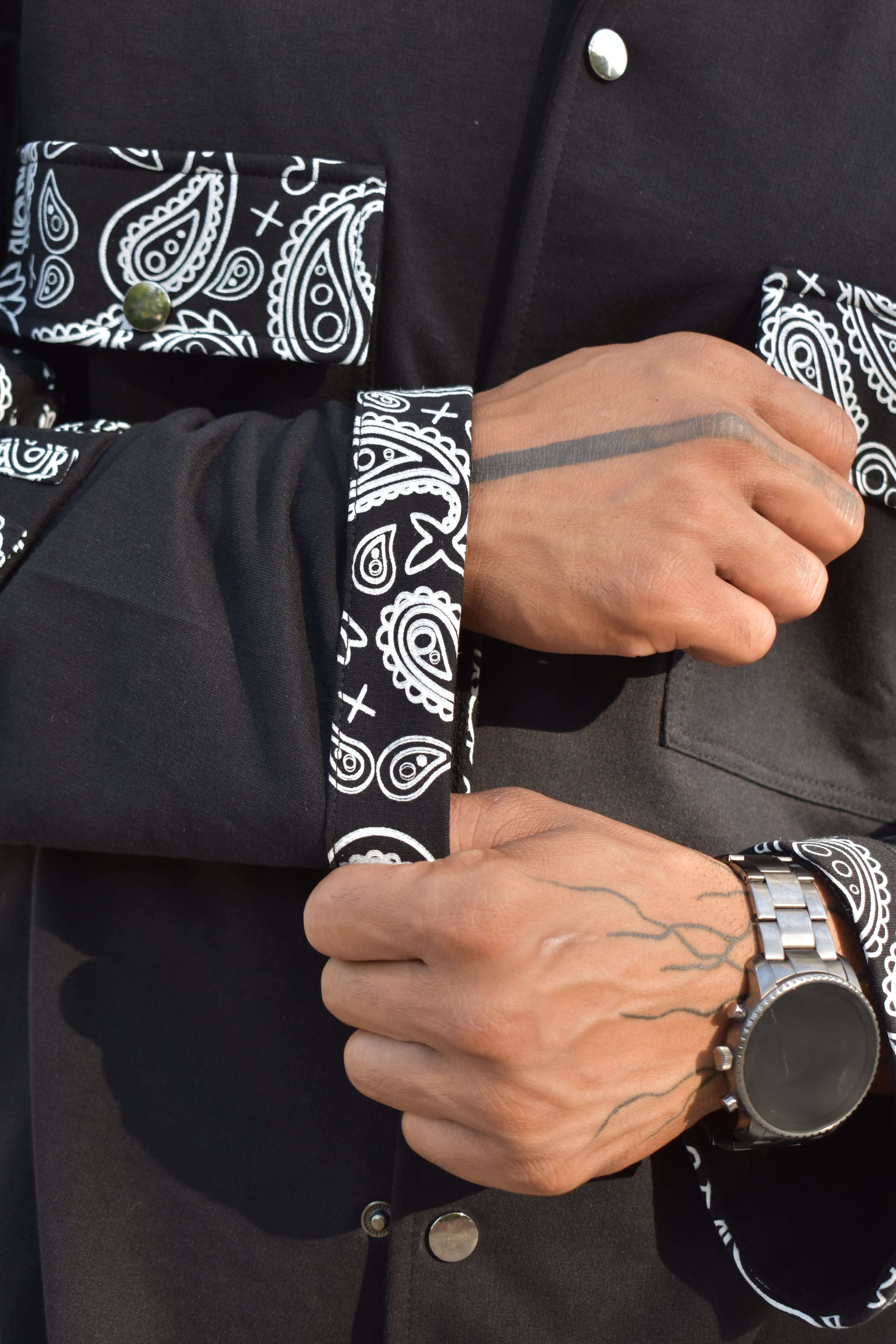 Close-up of a person adjusting the sleeve of a black Sanganeri shirt with intricate paisley patterns from DUDS.