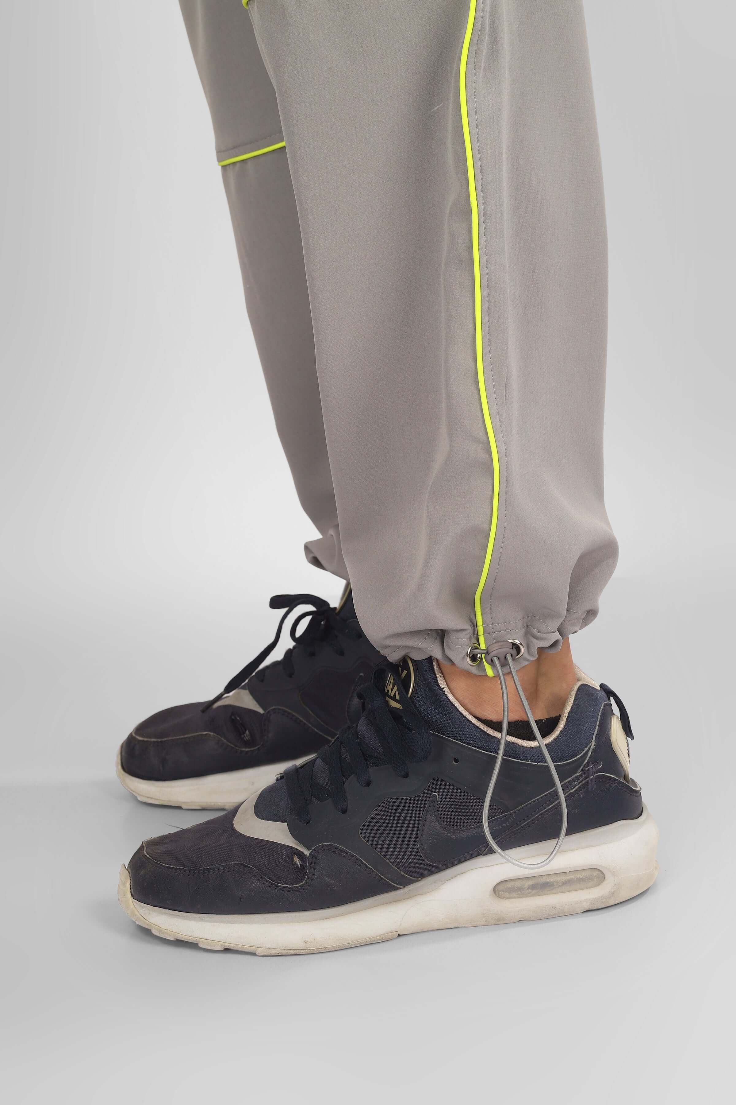 Close-up of grey parachute cargo pants with neon trim and drawstring detail, paired with black sneakers.