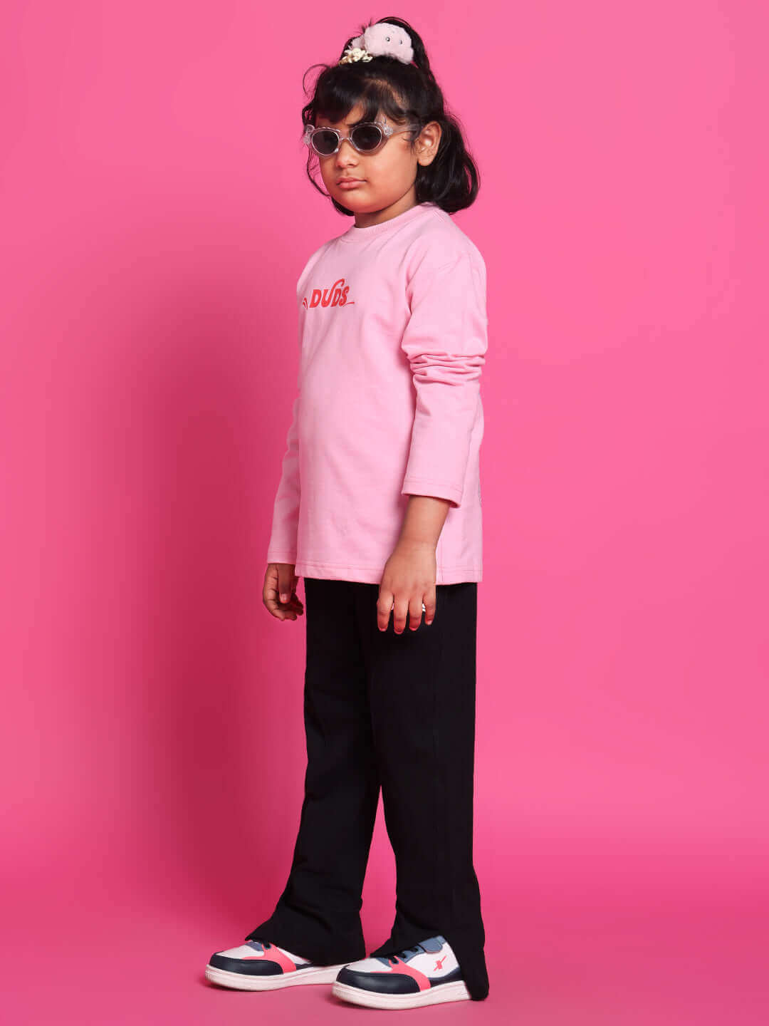 Child wearing pink scooter co-ord set from DUDS, featuring a pink top and black pants, standing against a pink background.