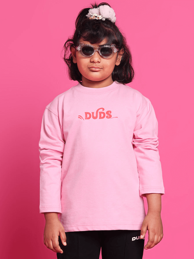Child wearing pink scooter oversized sweatshirt by DUDS, standing against a matching pink background, showcasing comfortable and stylish kids fashion.