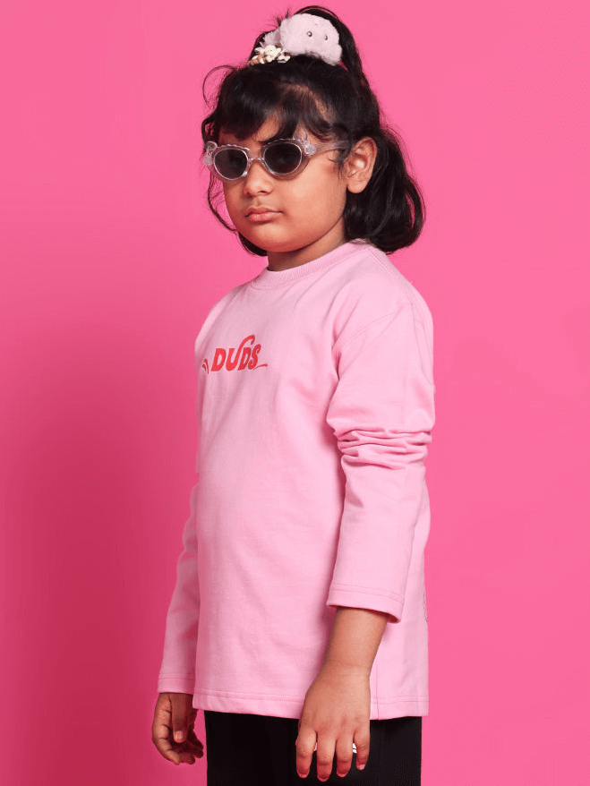Child wearing pink oversized sweatshirt by DUDS, with sunglasses, against a pink background.