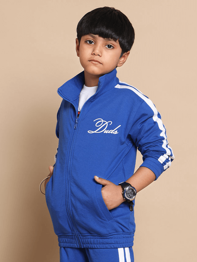 Boy wearing a royal blue Scotia jacket by Duds, featuring white stripes and embroidered logo, ideal for boys and girls.