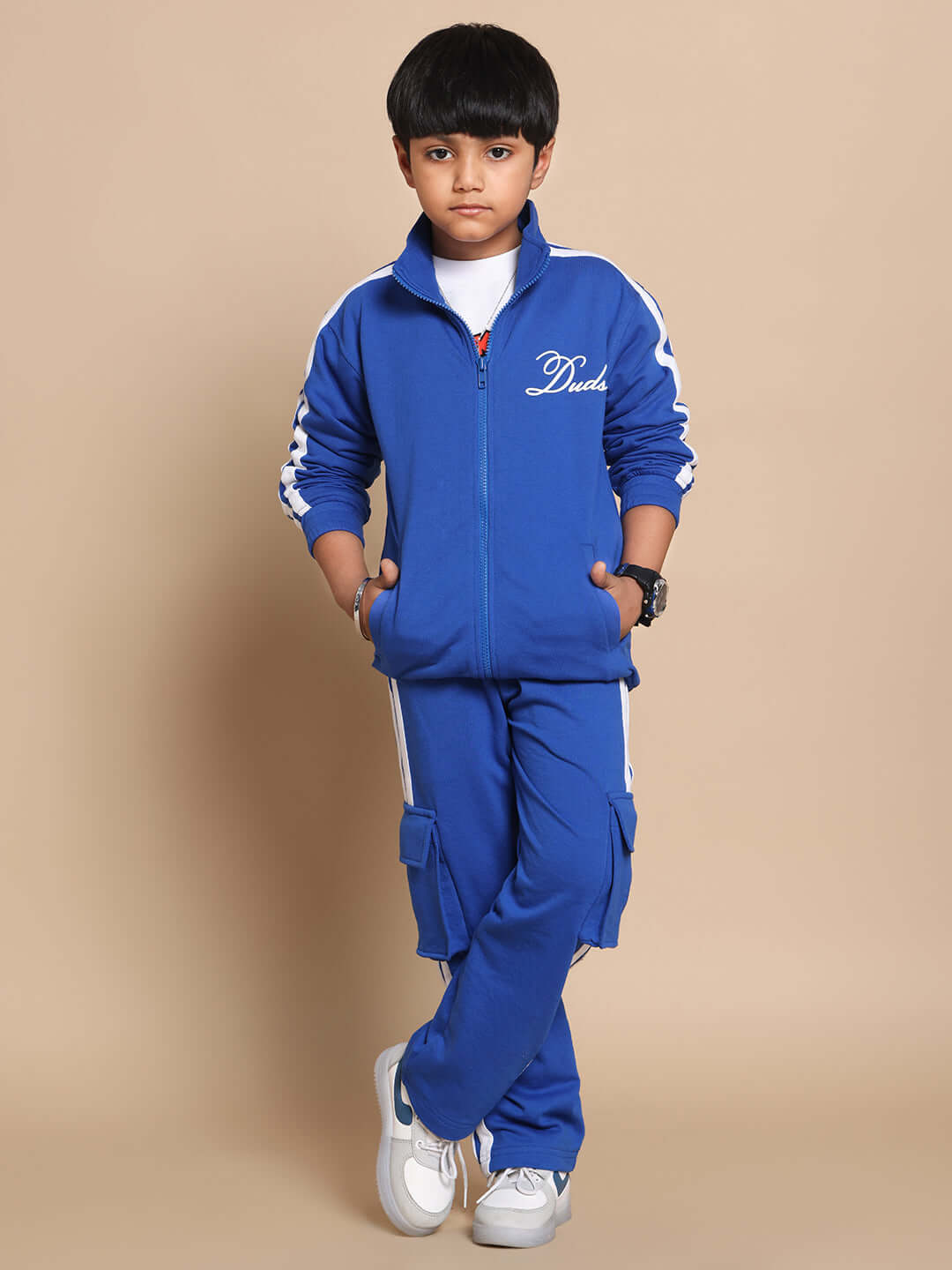 Child wearing Scotia Co-ord Set in royal blue, featuring a zip-up jacket and cargo pants, 100% cotton terry fabric, standing against a beige background.