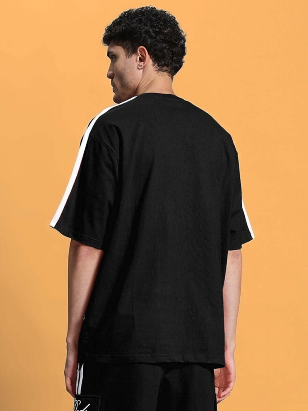 Back view of SCOTIA OVER-SIZED T-SHIRT BLACK in premium heavy gauge fabric and cotton blend, worn by a model against an orange background.