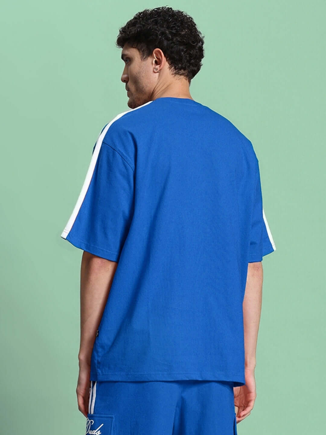 Model wearing SCOTIA OVER-SIZED T-SHIRT BLUE made of premium heavy gauge fabric, showing back view against a green background.